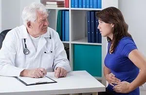 Woman talking to doctor while holding her stomach in pain